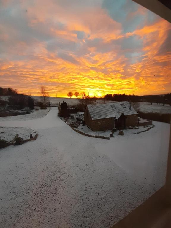 班科里Boghead Cottage: Holiday Cottage in Royal Deeside的雪中的房子,背景是日落