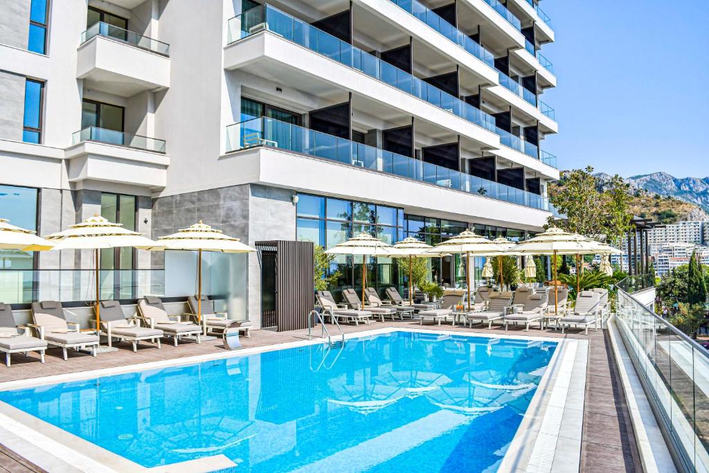 布德瓦Katamare Hotel的一张酒店游泳池的图片,里面摆放着椅子和遮阳伞