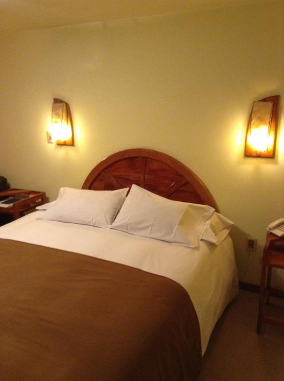 胡利亚卡Royal Inn Hotel Juliaca的卧室配有一张大床,墙上有两盏灯