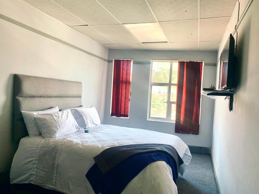 RandfonteinStay Inn Lodge Randfontein的一间卧室配有床和两个带红色窗帘的窗户。