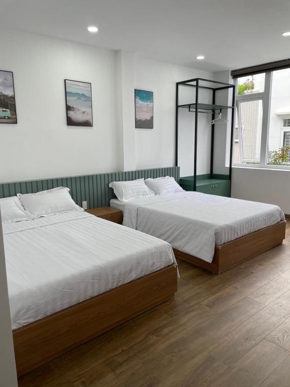 岘港Airport homestay的配有白色墙壁和木地板的客房内的两张床