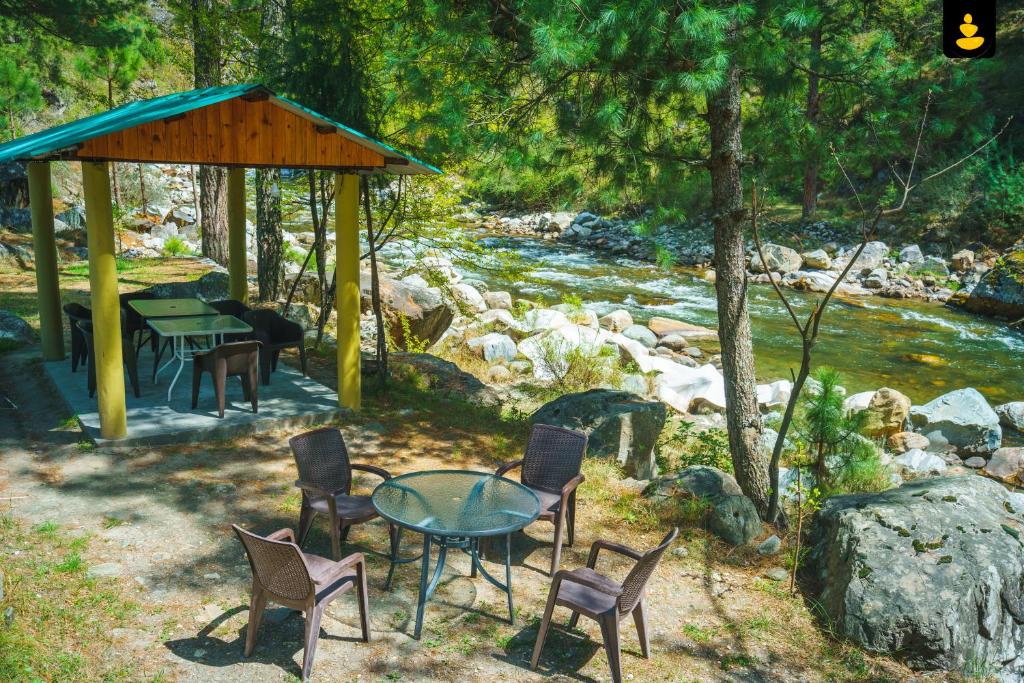 本贾尔LivingStone Backwater Resort Tirthan Valley的河边的桌椅,带凉亭