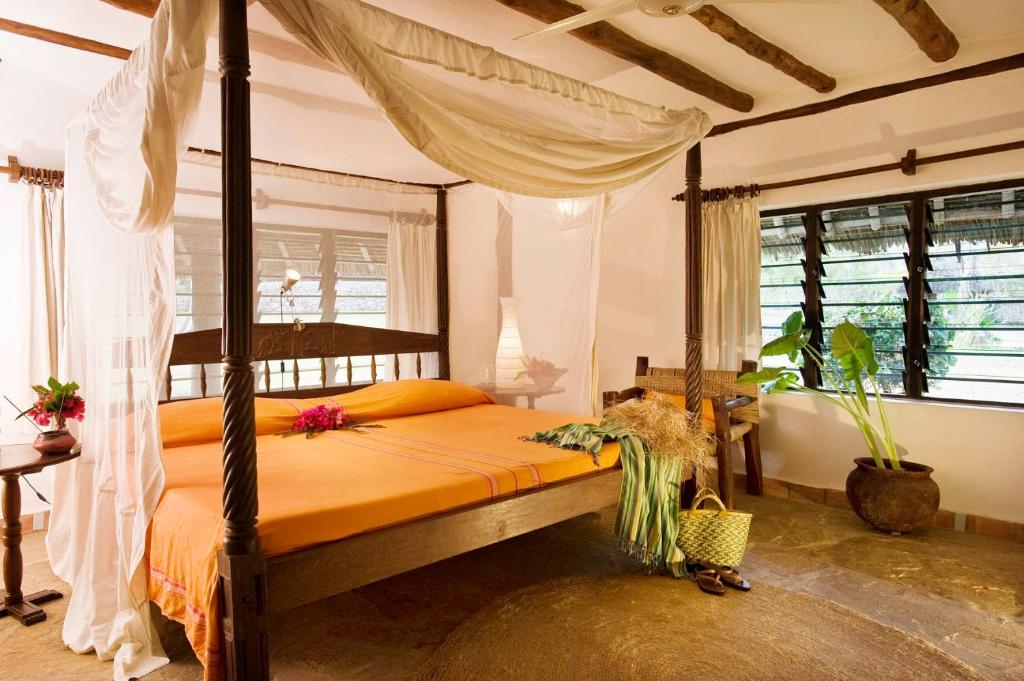 迪亚尼海滩Diani Marine Divers Village的一间卧室配有带橙色床单的天蓬床