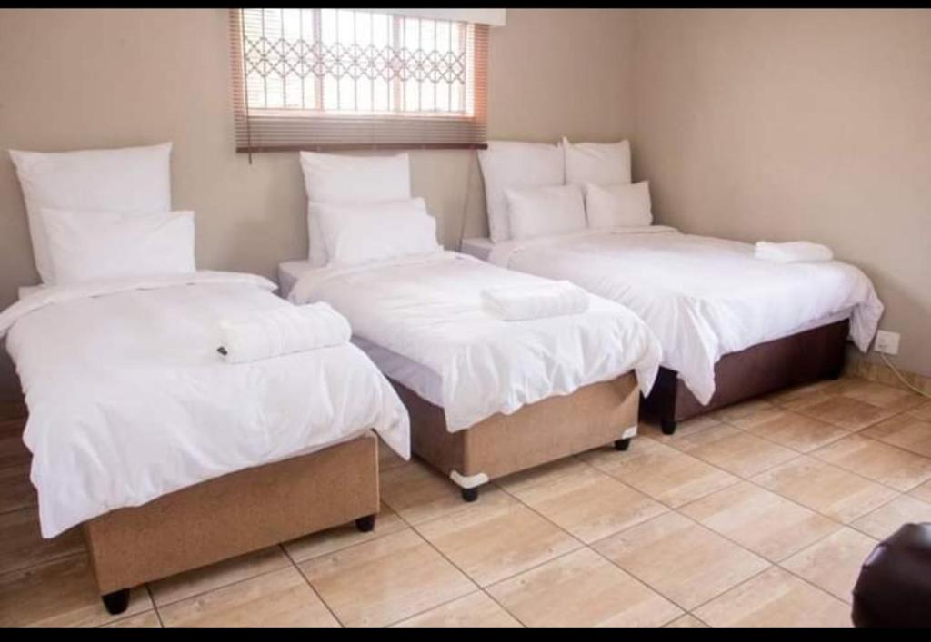 彼得马里茨堡Fairfield Guest House的客房设有三张床、白色床单和窗户。