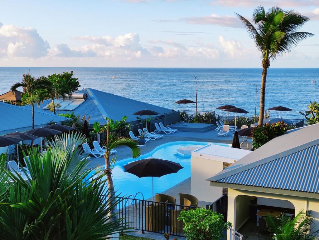 圣皮埃尔Hotel Exsel Victoria的毗邻大海的带椅子和遮阳伞的游泳池
