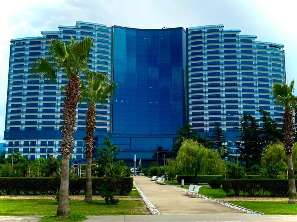 巴统Grand Bellagio Batumi Convention & Casino Hotel的一座高大的蓝色建筑,前面有棕榈树