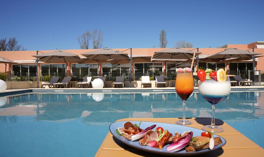 鲁塞Mount Venturi - Aix-En-Provence Sainte-Victoire - Bar & Restaurant & Padel的池畔餐桌上放着一盘食物和两杯饮料