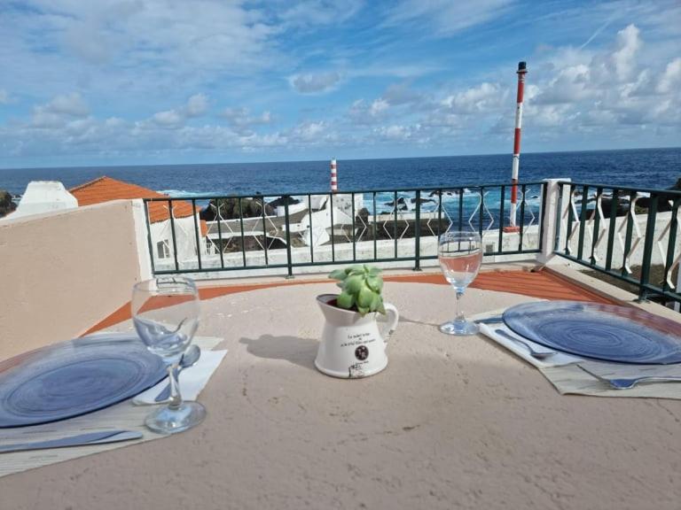 圣克鲁什达什弗洛里什"Apartamentos do Farol" com vista para o mar的阳台上的桌子和两杯葡萄酒