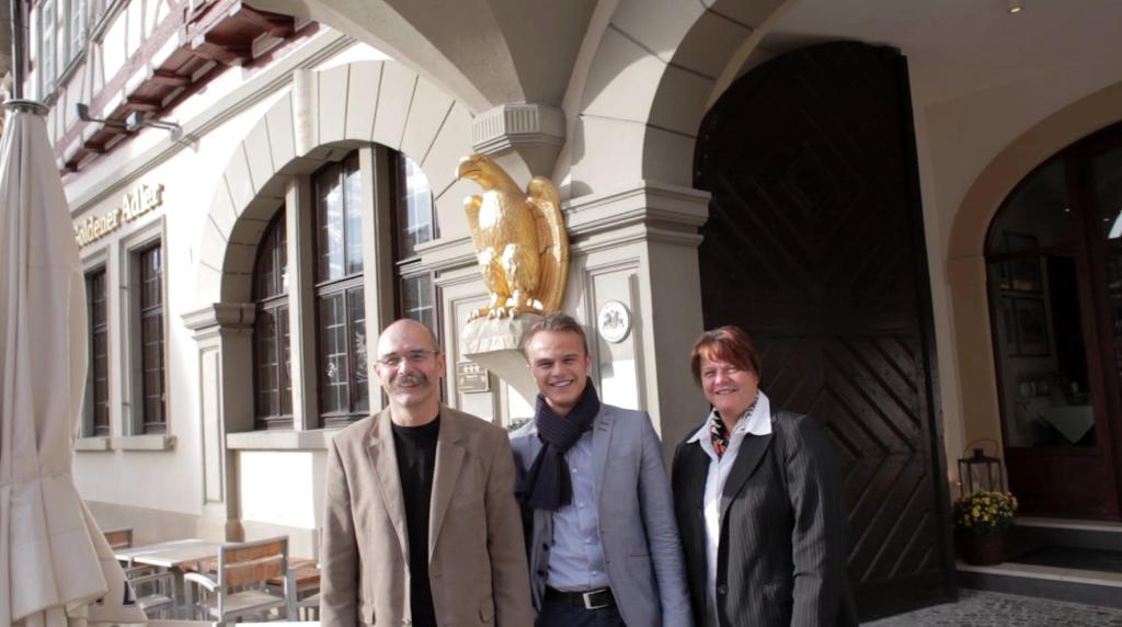 施韦比施哈尔戈尔登阿德勒斯塔德古特酒店的站在建筑物前面的两名男子和一名妇女