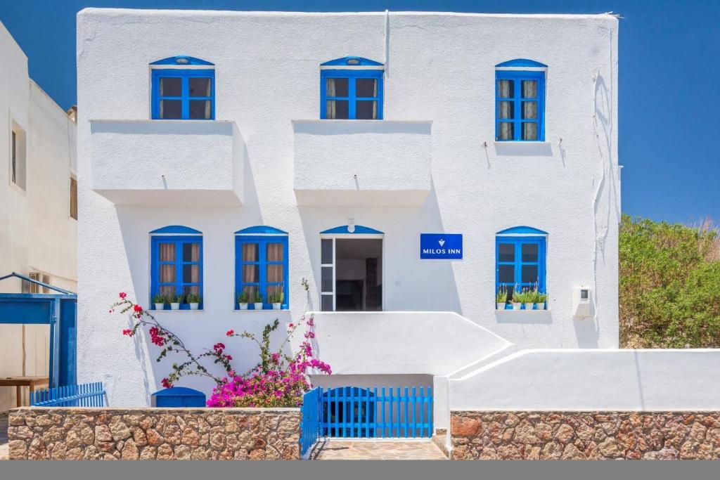阿达玛斯Milos Inn的白色的建筑,有蓝色的窗户和鲜花