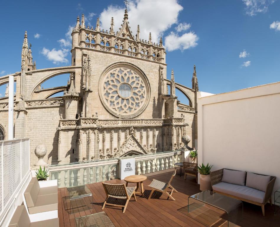 塞维利亚大教堂之门套房酒店的一个带椅子的阳台和一座带钟楼建筑
