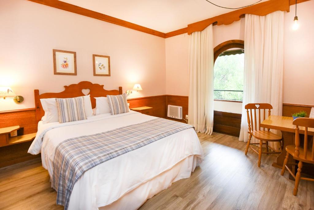 格拉玛多Hotel das Hortênsias的一间卧室配有一张床、一张桌子和一个窗户。
