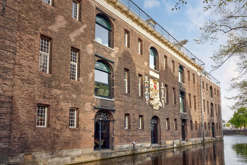 代尔夫特Hotel Arsenaal Delft的河边的一座大型砖砌建筑