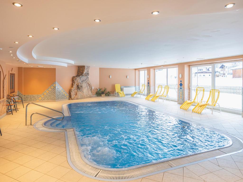 施特格Hotel Styrolerhof的一座大型游泳池,位于酒店客房内,配有黄色椅子