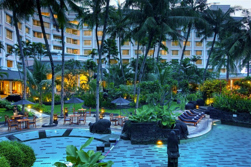 日惹Melia Purosani Yogyakarta的酒店庭院设有游泳池和桌椅