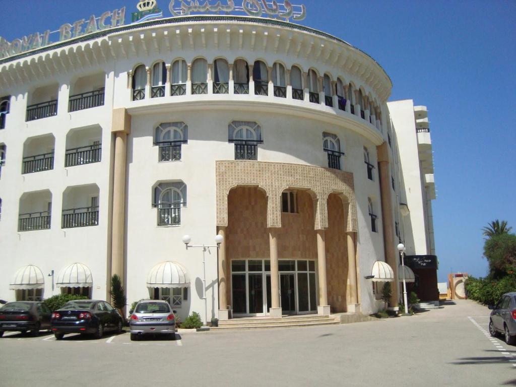 苏塞皇家海滩酒店的一座白色的大建筑,汽车停在停车场