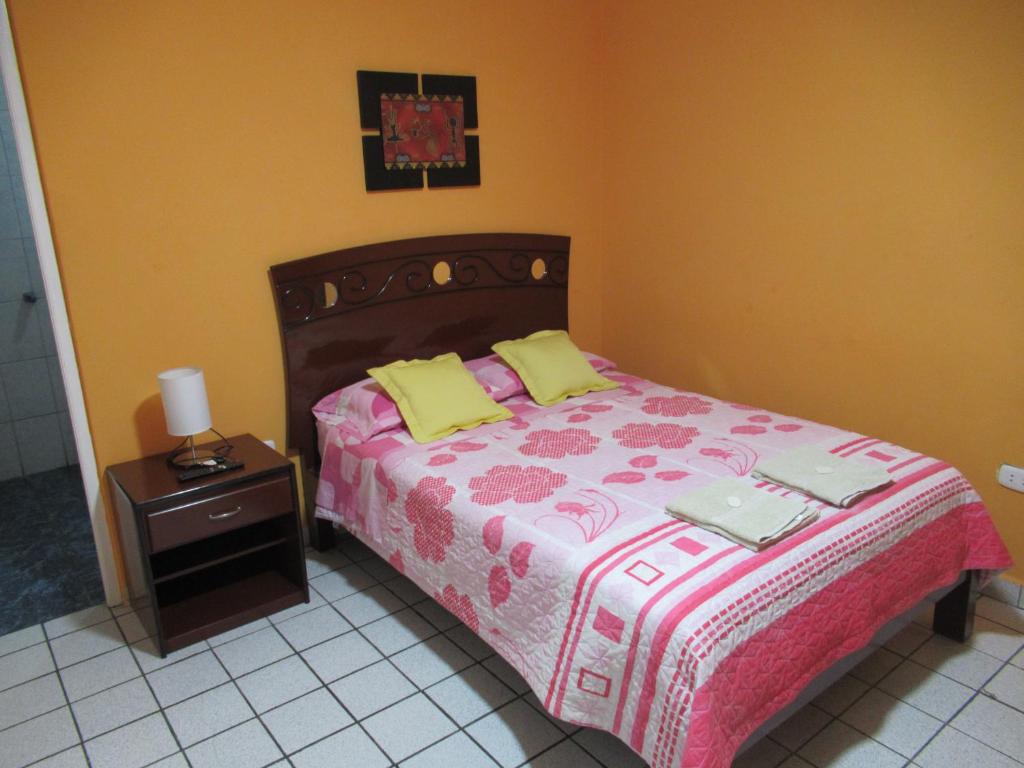 利马Kurmi Hostel Lima Airport的一间卧室配有一张床和一个带粉红色和黄色毯子的床头柜。