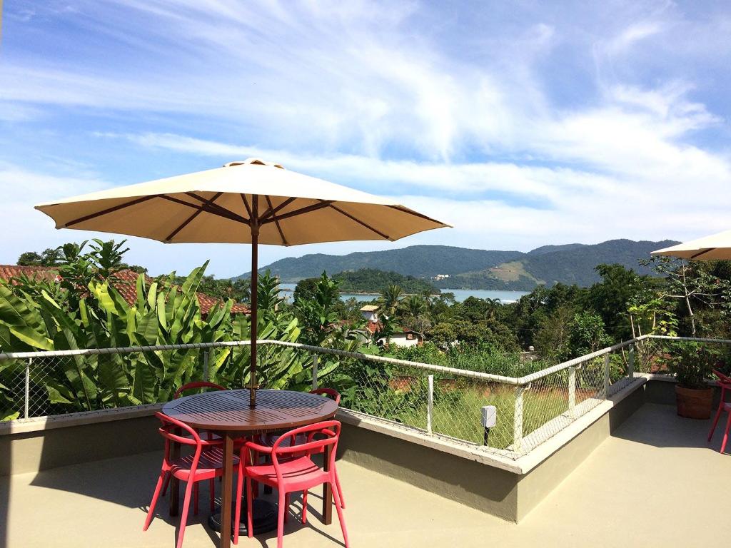 乌巴图巴Vila Praiana的阳台配有带2把椅子和遮阳伞的桌子