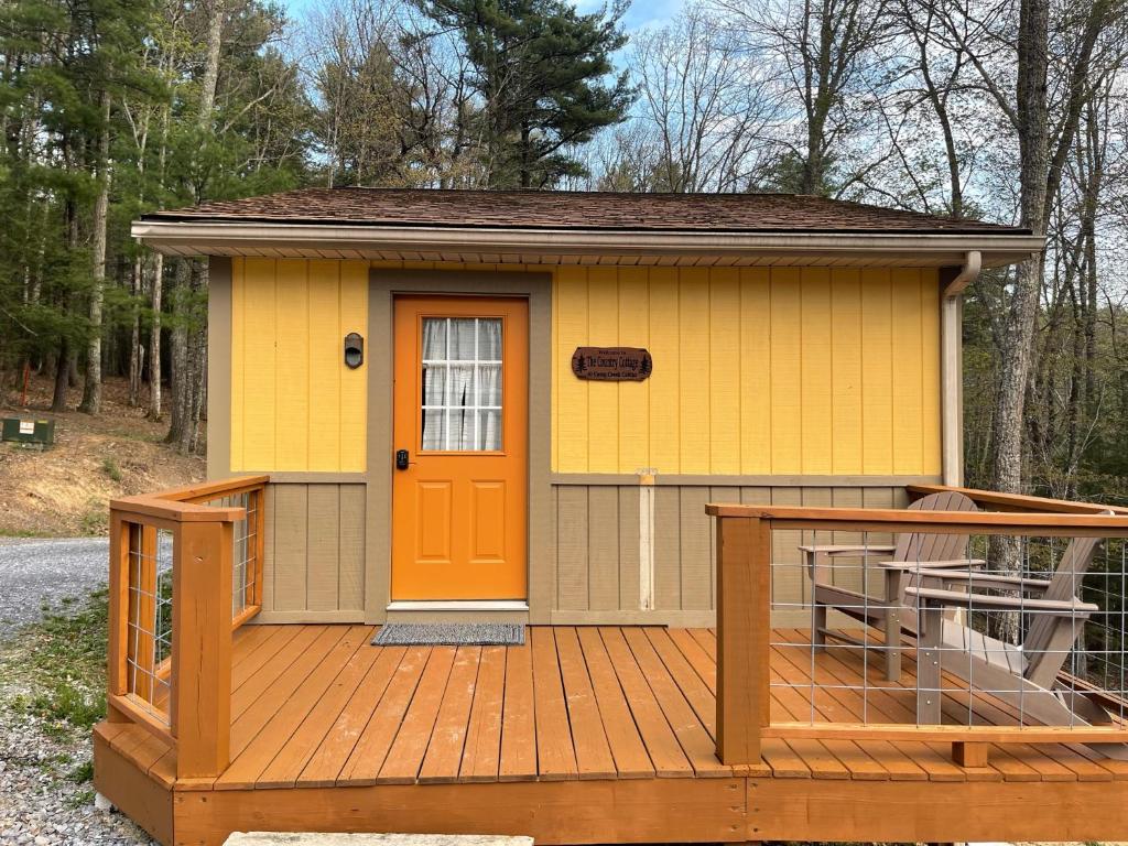 SpanishburgCountry Cottage at Camp Creek Cabins的一座黄色的小房子,甲板上设有橙色门