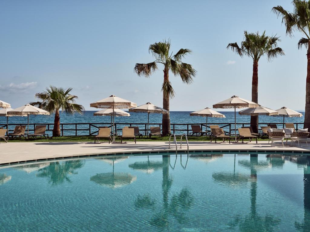 阿凯松Windmill Bay Hotel的一个带椅子和遮阳伞的游泳池以及大海