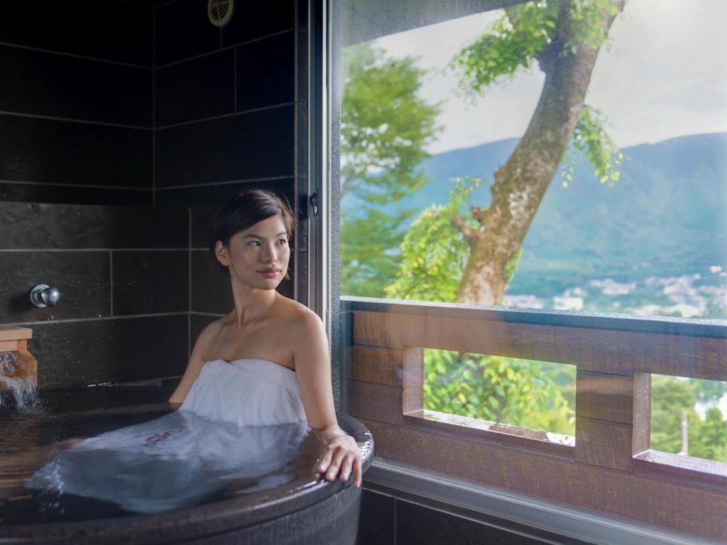 箱根LiVEMAX RESORT Hakone Sengokuhara的坐在浴缸里的女人,有窗子
