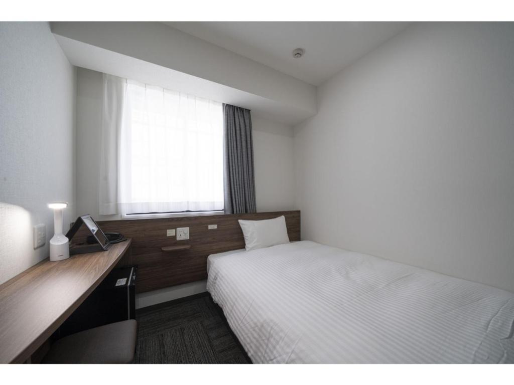 仙台R&B Hotel Sendai Higashiguchi - Vacation STAY 39921v的一间卧室配有一张床、一张书桌和一个窗户。