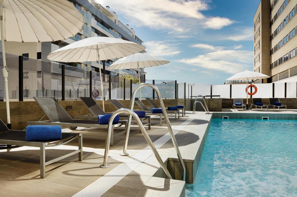 格拉纳达Gran Hotel Luna de Granada的一座带椅子和遮阳伞的大楼的顶部游泳池