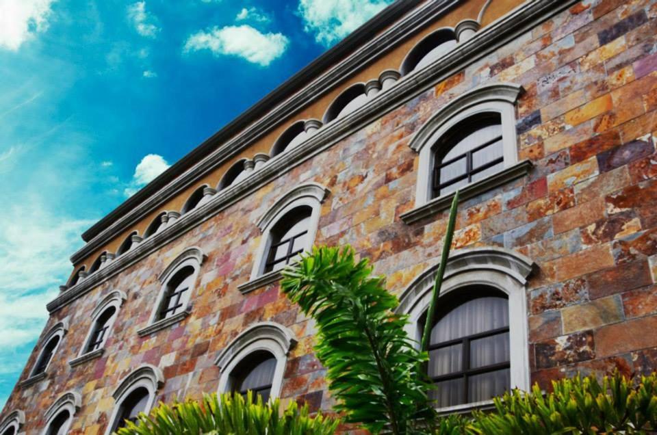 圣何塞圣约瑟雷亚尔广场套房公寓酒店的一座砖砌的建筑,设有窗户,并种植了棕榈树
