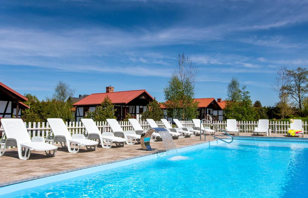 达尔沃沃Domki Dzika Róża的游泳池设有白色躺椅,旁边还有人站在游泳池旁