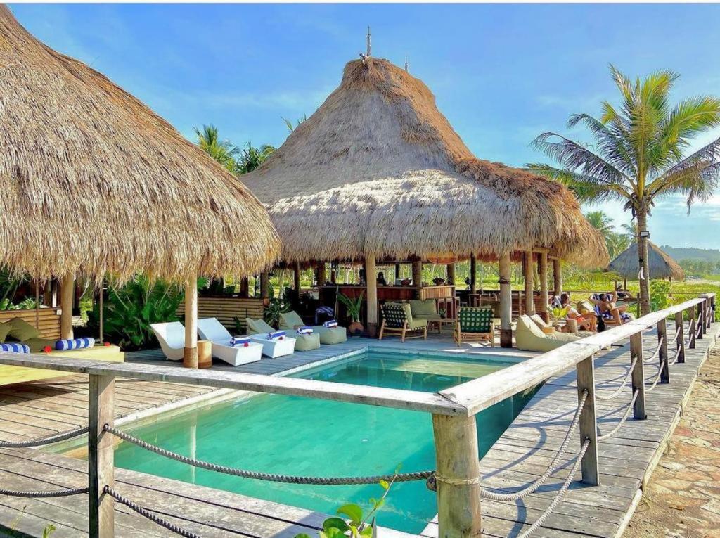 怀卡布巴克Sumba Beach House的一个带游泳池和茅草遮阳伞的度假村