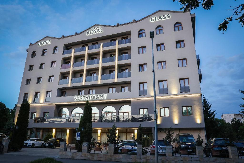 克卢日-纳波卡Royal Class Hotel的一座白色的大建筑,汽车停在停车场