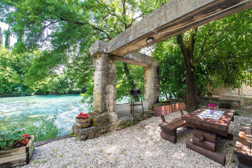 BunaCharming Cottage的河边的石制凉亭,配有桌子和长凳