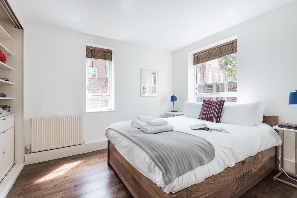 伦敦Bright and stylish apartment in trendy Islington by UnderTheDoormat的白色卧室设有一张大床和两个窗户