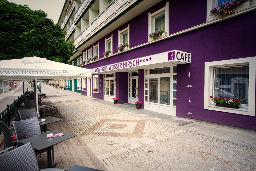 玛利亚采尔AKTIVHOTEL Weisser Hirsch的一条街道上带桌子和遮阳伞的紫色建筑