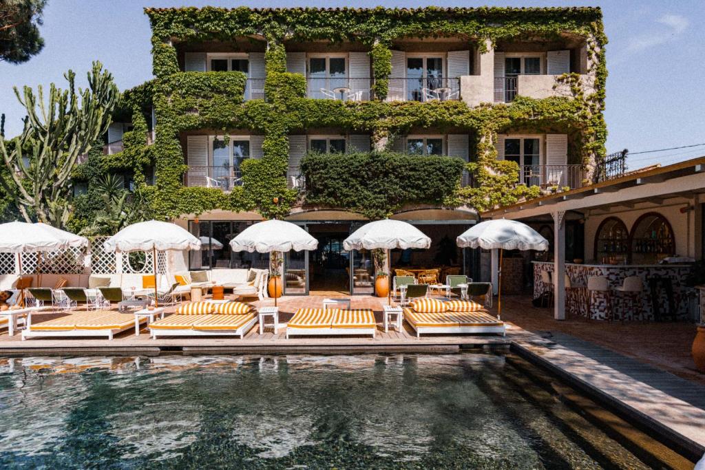 圣特罗佩Hotel des Lices的游泳池旁的酒店拥有椅子和遮阳伞