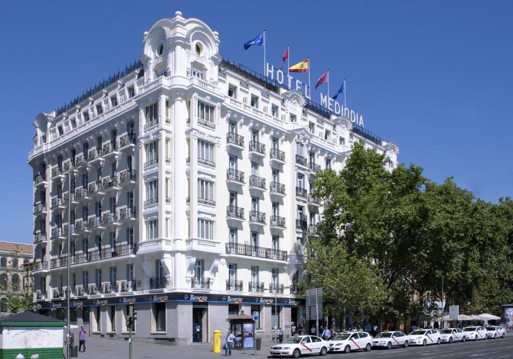 马德里正午酒店的一座白色的大建筑,前面有汽车停放