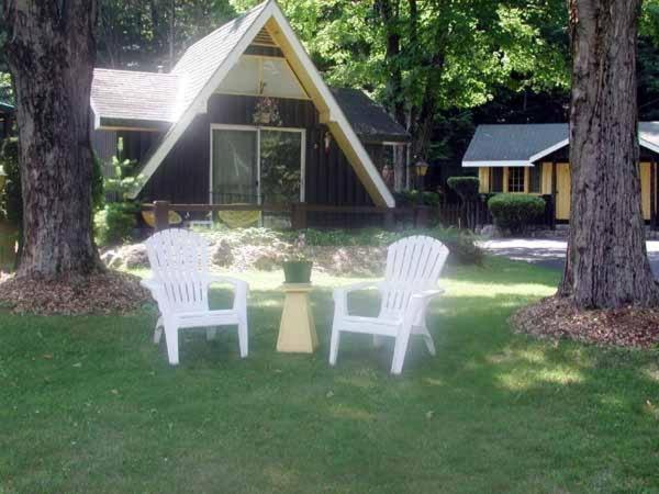 乔治湖Amber Lantern Two-Bedroom Cottage的坐在房子前面的草上,有三把白色椅子
