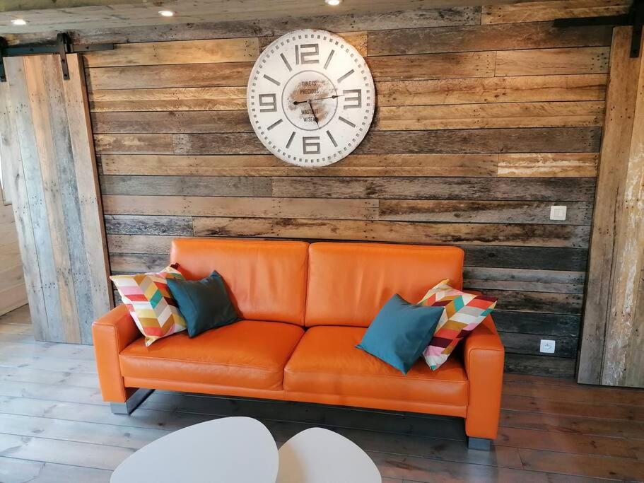 赫尔Le canard: rustig genieten aan het water的橙色的沙发,配有枕头,墙上挂着时钟