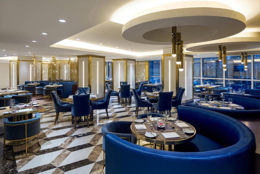 麦加Sheraton Makkah Jabal Al Kaaba Hotel的餐厅设有蓝色的椅子和桌子以及窗户。