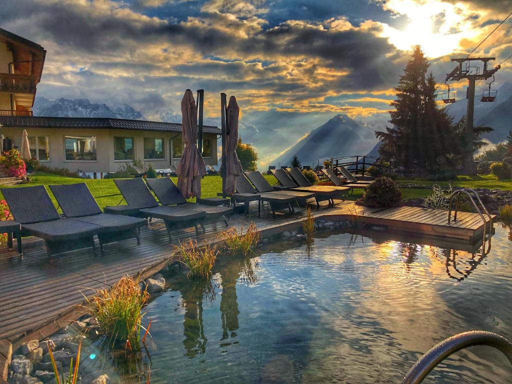 比尔塞贝格Alpinresort Schillerkopf的一个带椅子的庭院和一个享有日落美景的游泳池