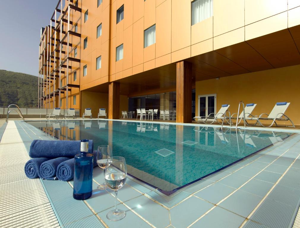 格拉纳达马西亚阿尔罕布拉皇宫酒店的一座游泳池,旁边是一座建筑,配有酒杯和椅子