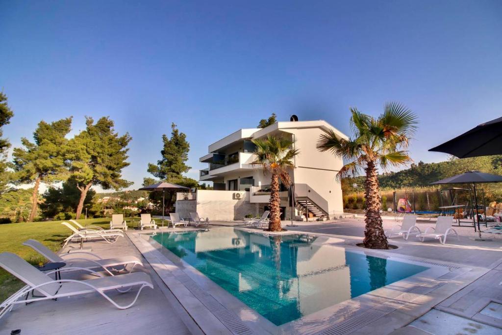 波利克罗诺Pine Resort的一座房子前面的游泳池,游泳池里摆放着椅子和棕榈树