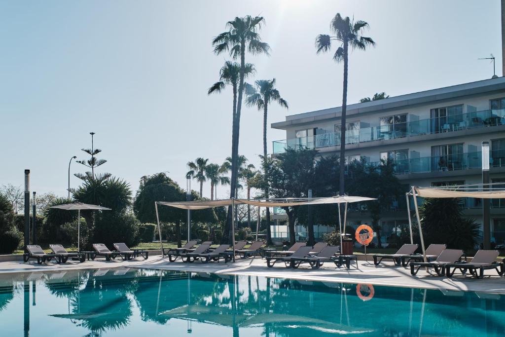 坎帕斯蒂利亚赫里奥马略卡酒店公寓的一座带椅子和遮阳伞的游泳池位于一座建筑旁边