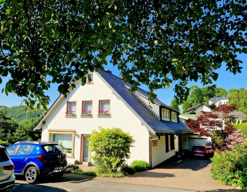 维林根Ferienwohnungen Tannenhof的白色的房子,有红色的窗户和蓝色的汽车