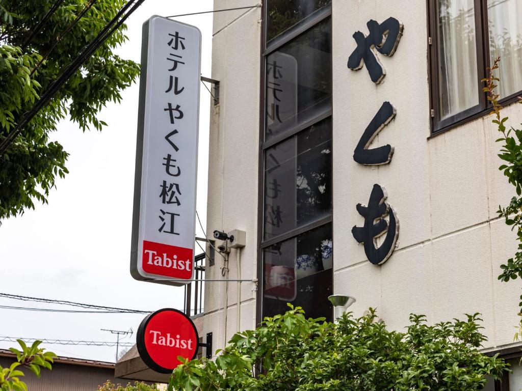 松江市Tabist Hotel Yakumo Matsue的建筑物边的标志,带有时钟