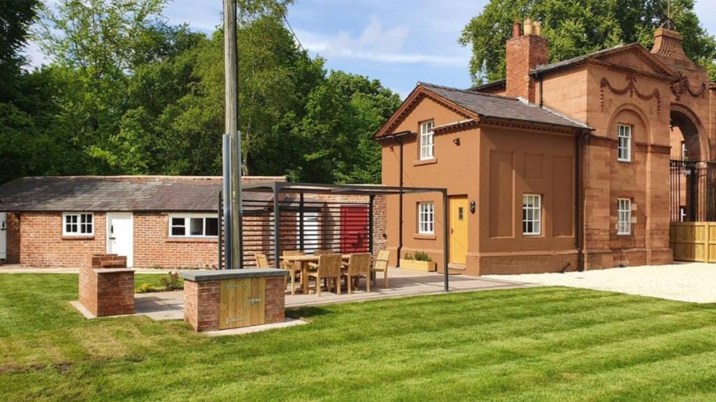 Little BudworthOulton Park Lodge的一座砖砌建筑,在院子里配有桌椅