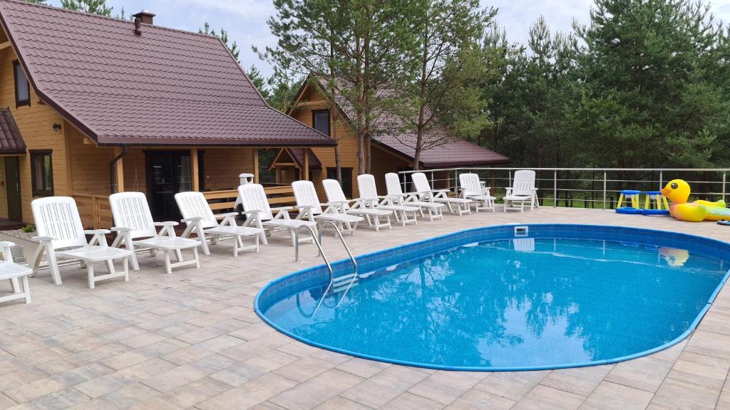 帕瑟姆Sosnowe Wzgórze的一个带白色椅子的游泳池以及一座房子