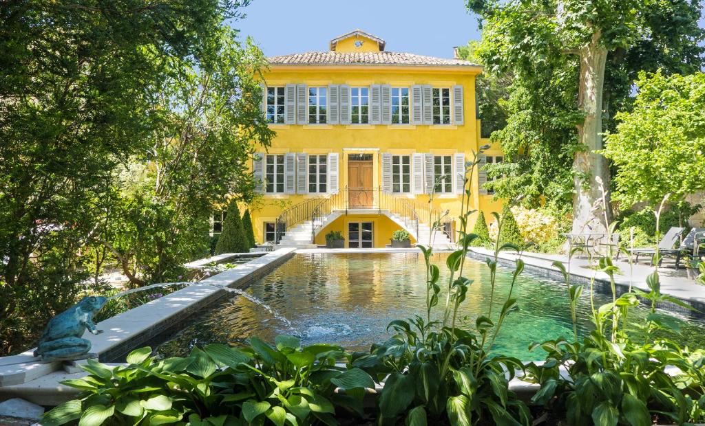 普罗旺斯艾克斯Villa Amara的一座黄色的建筑,前面有一个池塘