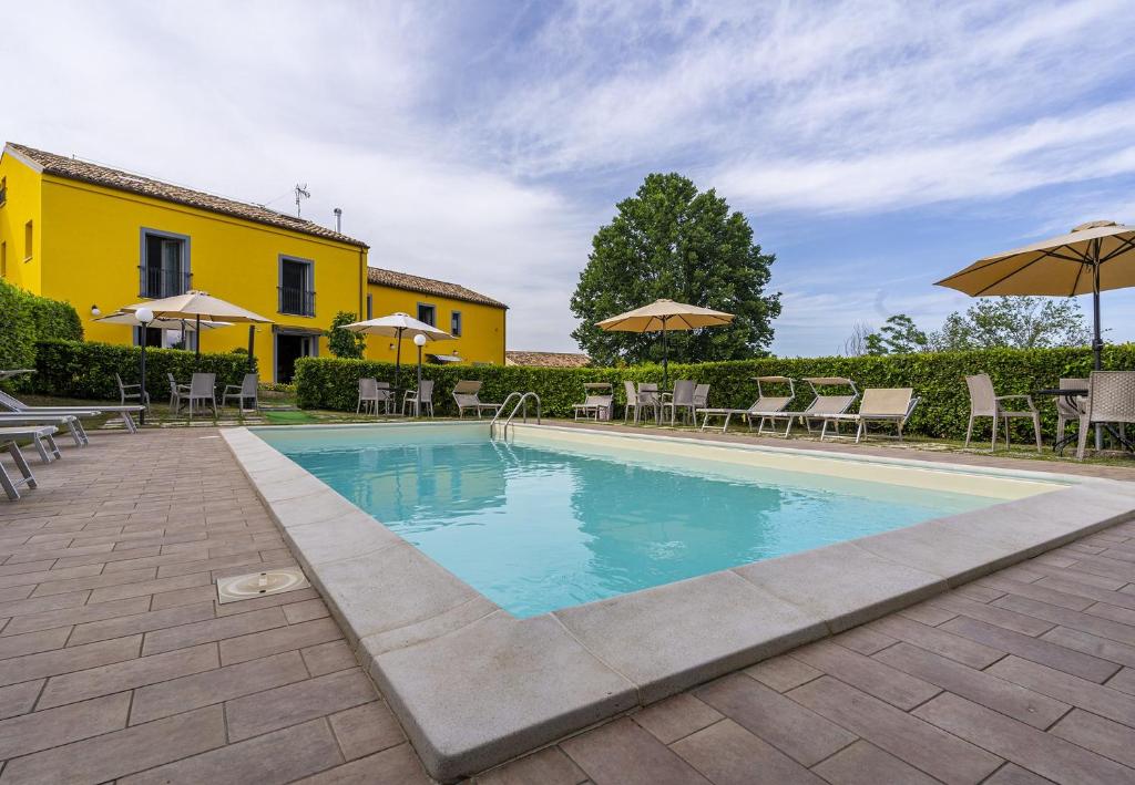 瑟萨帕洛姆L'Olmo di Casigliano的一座黄色建筑旁的游泳池,配有椅子和遮阳伞