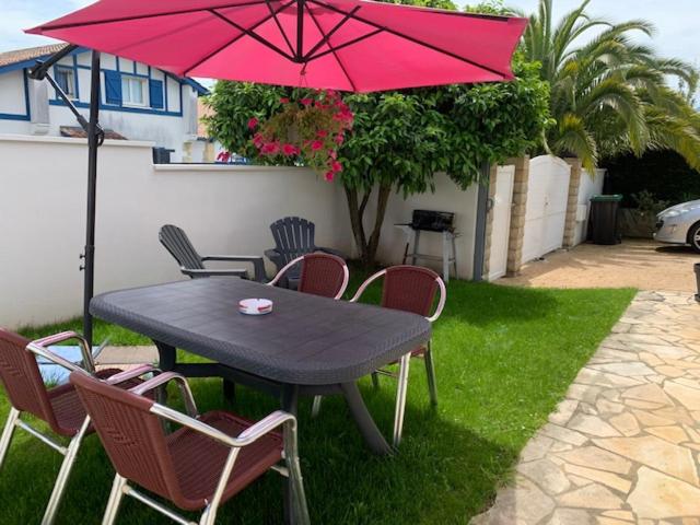 昂代APPARTEMENT LES HIRONDELLES 2KM PLAGE-WiFI-JARDIN-PARKING-DRAPS ET SERVIETTES的一张黑色桌子和椅子,配有粉红色的雨伞